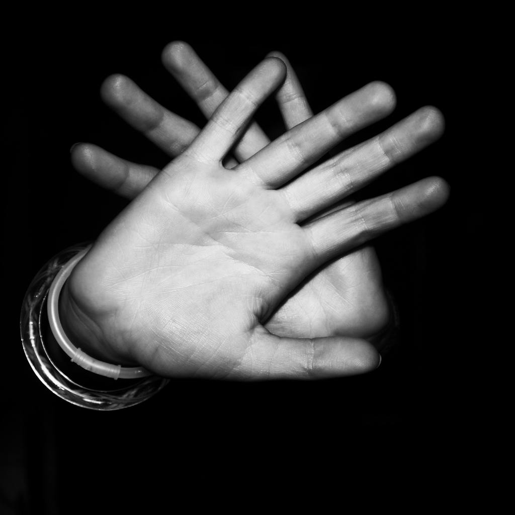 Monochrome close-up of hands in stop gesture against dark background.